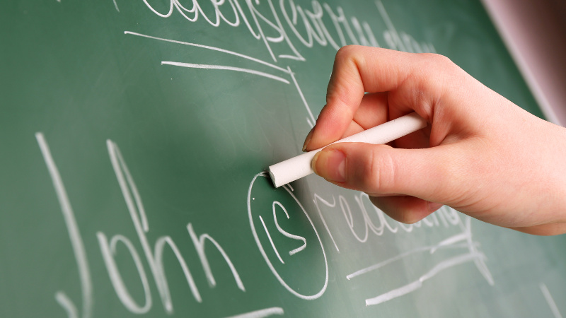 Teacher hand writing grammar sentences on blackboard background